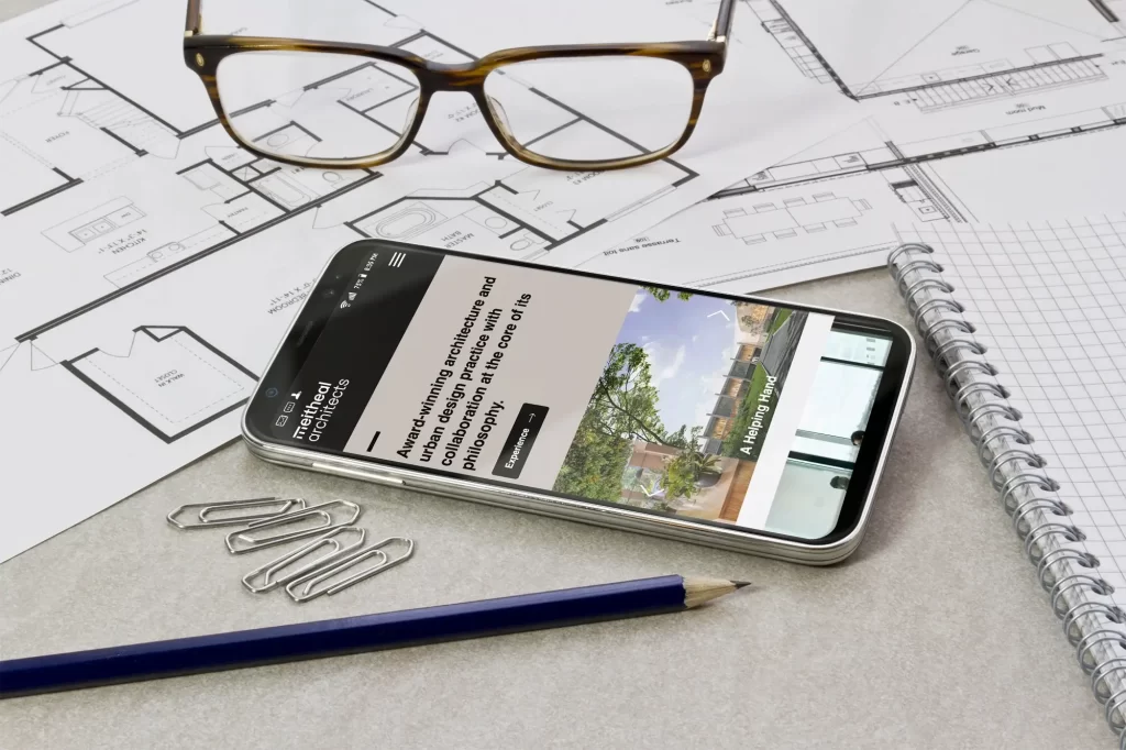 We Are Kaizen Meitheal Architects homepage on a mobile device placed on top of architectural plans